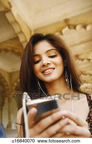Stock Image - Low angle view of a young woman looking at an MP3 player, Agra Fort, Agra, Uttar Pradesh, India. Fotosearch