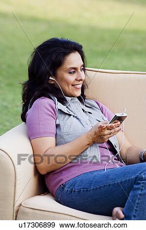 Stock Photo - Mid adult woman sitting in an armchair and listening to an MP3 player. Fotosearch