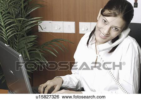 Stock Photograph - Portrait of a receptionist talking on the telephone. Fotosearch