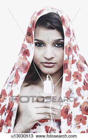 Stock Image - Portrait of a young woman with a stole on her head listening to an MP3 player. Fotosearch