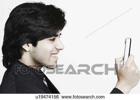 Stock Photograph - Side profile of a businessman operating a mobile phone. Fotosearch