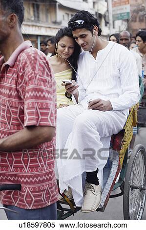 Stock Photography - Young couple sitting on a rickshaw and listening to an MP3 player. Fotosearch
