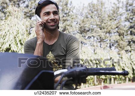 Stock Photo - Young man sitting on a motorcycle and using a mobile phone. Fotosearch