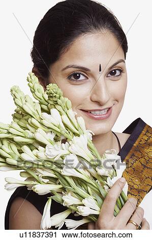 Stock Image - Portrait of a young woman wearing a sari and holding a bunch of flowers. Fotosearch