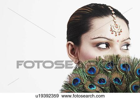 Close-up of a young woman holding a peacock feather fan over her face View Large Photo Image Stock Photo - Close-up of a young woman holding a peacock feather fan over her face. Fotosearch