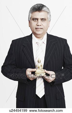 Stock Photo - Portrait of a mature man holding a statue of Buddha. Fotosearch