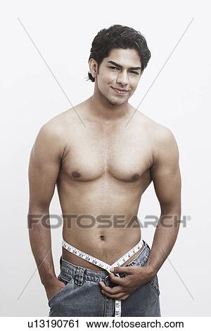 Stock Image - Portrait of a young man measuring his waist with a measuring tape. Fotosearch