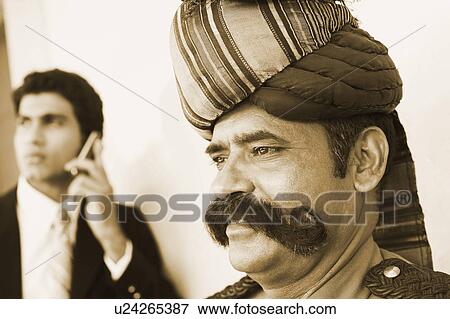 Stock Photo - Close-up of a security guard with a businessman talking on a mobile phone behind him. Fotosearch