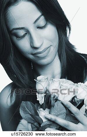 Stock Image - Close-up of a young woman looking at a bouquet of roses. Fotosearch