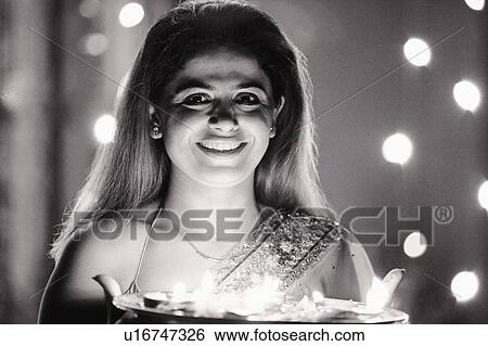 Stock Photograph - Portrait of a mid adult woman holding oil lamps in a plate and smiling. Fotosearch