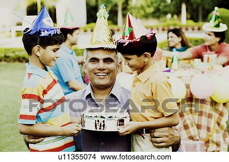 Two boys standing with their father and holding a birthday cake View Large Photo Image Picture - Two boys standing with their father and holding a birthday cake. Fotosearch