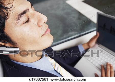 Stock Image - Close-up of a businessman wearing a hands free device and holding a laptop. Fotosearch