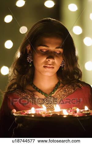 Stock Photo - Close-up of a young woman holding oil lamps in a plate. Fotosearch