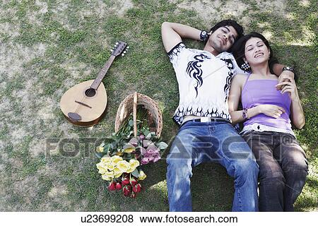 Stock Photo - High angle view of a young couple lying together in the park. Fotosearch