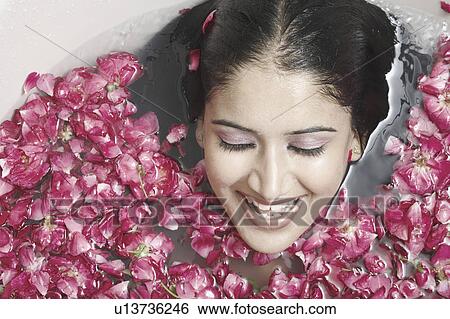 Stock Photograph - High angle view of a young woman lying in a bathtub covered with flower petals. Fotosearch