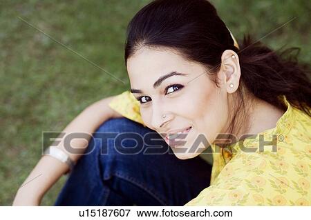 Stock Photo - Portrait of a young woman sitting in a lawn and smiling. Fotosearch