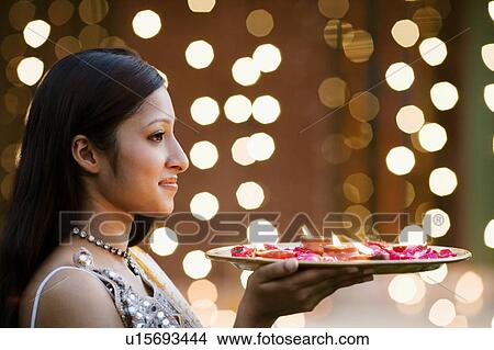 Side profile of a young woman holding oil lamps and Rose petals in a plate View Large Photo Image Picture - Side profile of a young woman holding oil lamps and Rose petals in a plate. Fotosearch