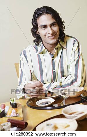 Stock Image - Portrait of a young man sitting at the dining table and smiling. Fotosearch