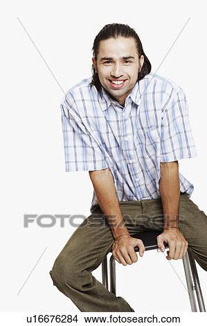 Picture - Portrait of a young man sitting on a stool and smiling. Fotosearch