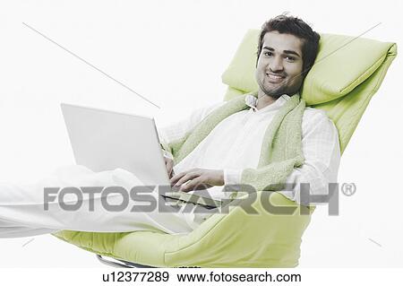 Stock Photo - Portrait of a young man sitting with a laptop. Fotosearch