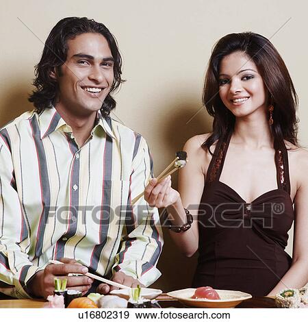 Stock Photo - Portrait of a young couple sitting at the dining table and smiling. Fotosearch