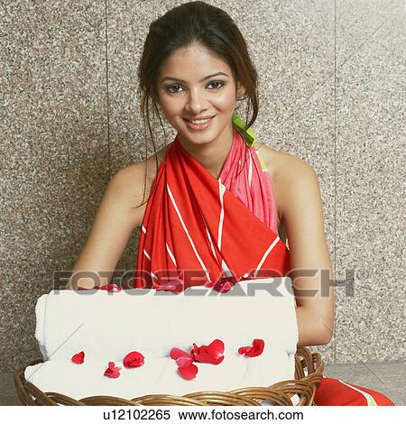 Stock Photography - Portrait of a young woman with a towel and rose petals in a wicker basket. Fotosearch