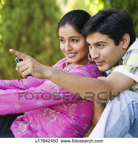 Stock Image - Side profile of a young woman sitting with a young man pointing forward. Fotosearch
