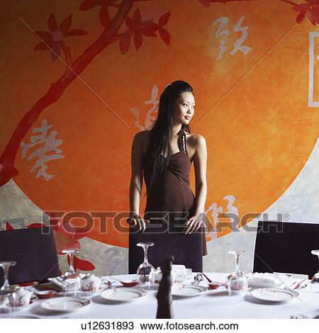 Stock Image - Young woman standing behind a table in a restaurant. Fotosearch