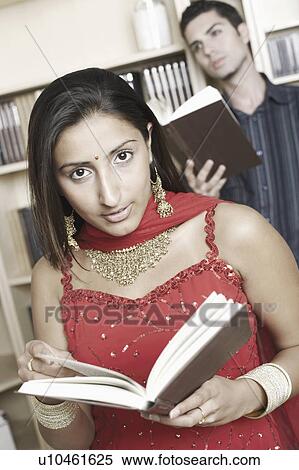 Stock Photography - Portrait of a young woman holding a book with a young man standing behind her. Fotosearch