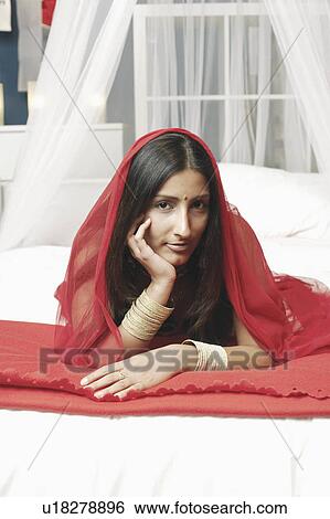 Portrait of a young woman lying on the bed with her hand on her chin View Large Photo Image Stock Photograph - Portrait of a young woman lying on the bed with her hand on her chin. Fotosearch