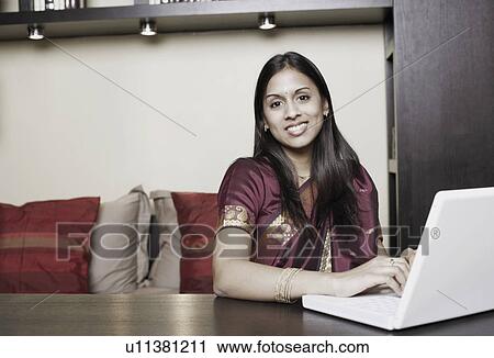 Stock Image - Portrait of a young woman sitting in front of a laptop. Fotosearch