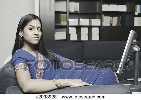 Portrait of a young woman sitting on a couch in front of a computer monitor View Large Photo Image Stock Image - Portrait of a young woman sitting on a couch in front of a computer monitor. Fotosearch