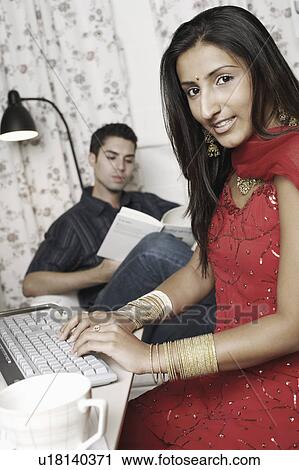 Portrait of a young woman working on a computer with a young man reading a book behind her View Large Photo Image Stock Image - Portrait of a young woman working on a computer with a young man reading a book behind her. Fotosearch