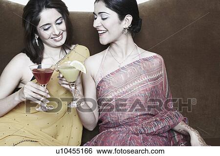 Two young women sitting on a couch toasting with martini glasses View Large Photo Image Stock Photograph - Two young women sitting on a couch toasting with martini glasses. Fotosearch