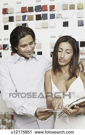 Stock Image - Young couple choosing fabric swatches from a magazine. Fotosearch