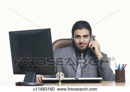 Portrait of a businessman talking on a cordless phone in front of a computer View Large Photo Image Stock Image - Portrait of a businessman talking on a cordless phone in front of a computer. Fotosearch