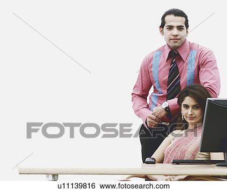 Stock Photograph - Portrait of a businesswoman sitting with a businessman standing beside her in an office. Fotosearch
