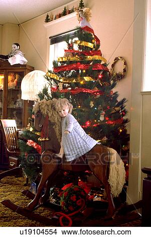 Picture - Doll riding rocking horse beside Christmas tree. Fotosearch