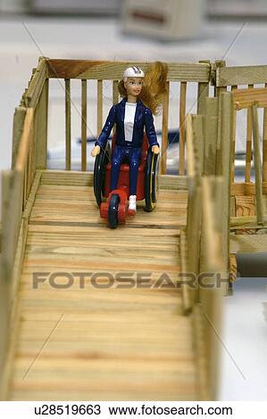Stock Image - Barbie in a wheelchair on a doll sized wooden ramp.. Fotosearch