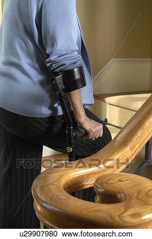 Stock Image - Lady with arm crutches walks upstairs.. Fotosearch