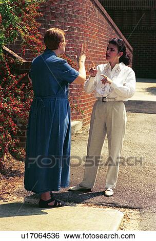 Stock Photograph - Two women, both deaf or with hearing impairments, conversing via sign language outside a building following a seminar.. Fotosearch