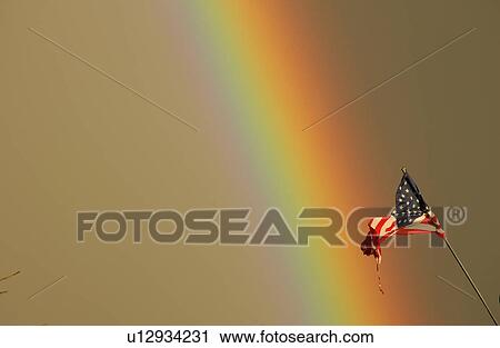 Stock Image - American flag swaying under a rainbow. Fotosearch