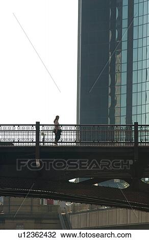 Person standing on a bridge next to a high rise building in Chicago View Large Photo Image Stock Image - Person standing on a bridge next to a high rise building in Chicago. Fotosearch