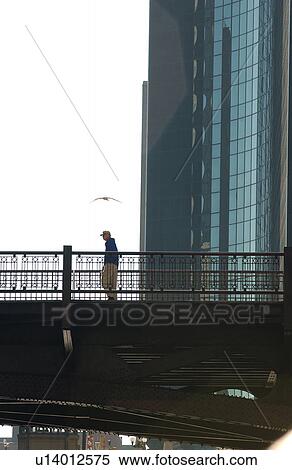 Person standing on a bridge next to a high rise building in Chicago View Large Photo Image Stock Photography - Person standing on a bridge next to a high rise building in Chicago. Fotosearch