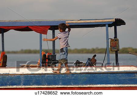Stock Image - Young boy walking along edge of a boat in Cambodia. Fotosearch