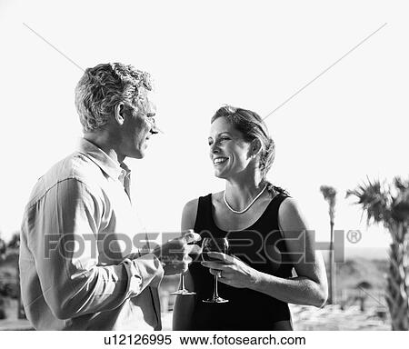 Stock Photography - couple holding wine glasses and smiling at each other. Fotosearch