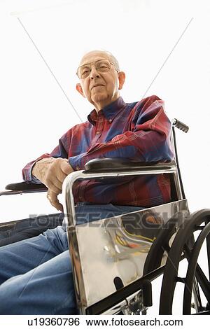 Stock Photograph - Low-angle view of an elderly man sitting in wheelchair looking down at viewer. Fotosearch