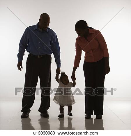 Stock Image - Man and woman standing holding up infant girl by her hands against white background. Fotosearch