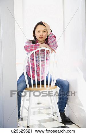 Stock Image - Pretty young woman sitting on chair at table in kitchen. Fotosearch