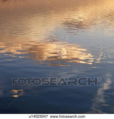 Stock Photo - Reflections of orange and yellow sunset on rippling water.. Fotosearch